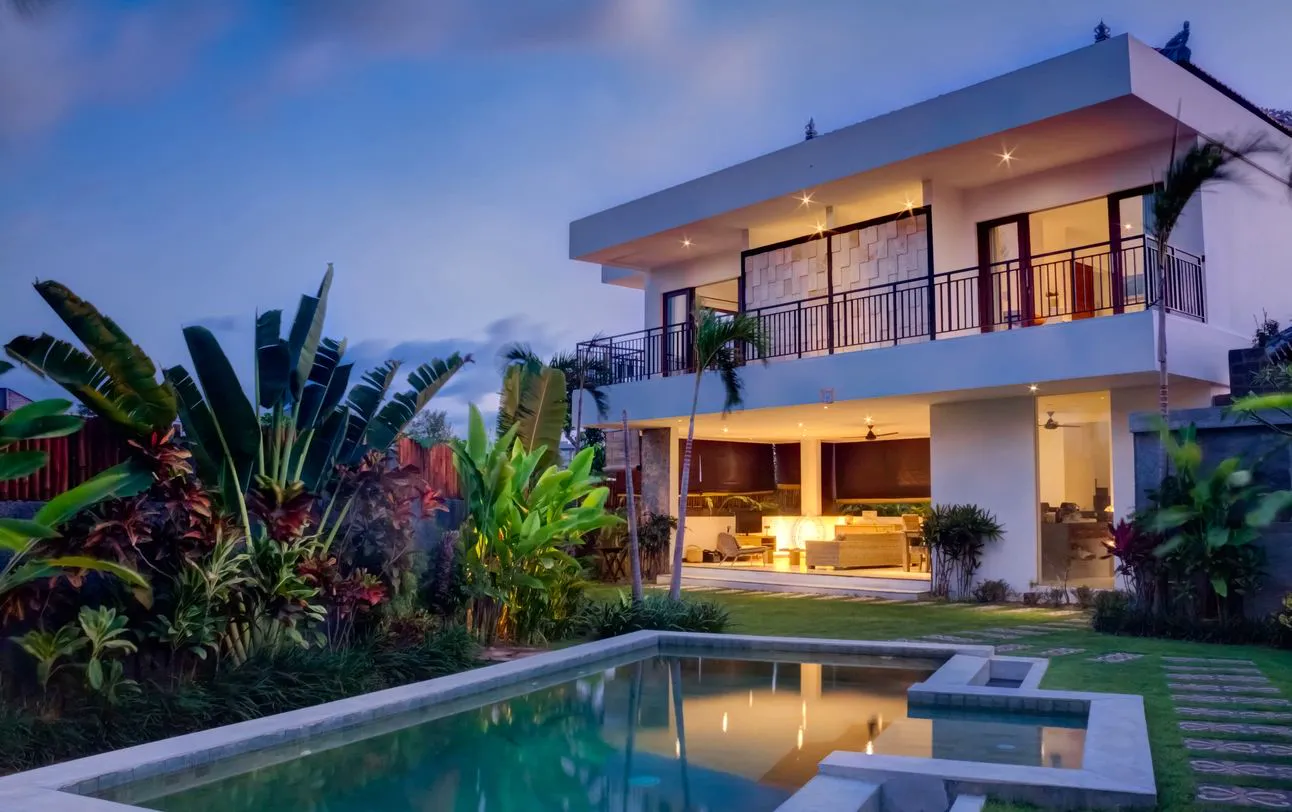 Contemporary home with a pool and tropical landscaping at dusk